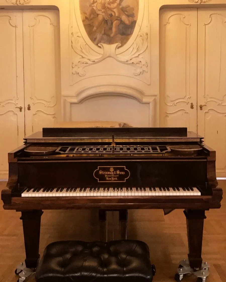 Krem rengi kabartmalı duvarları ve melek tablosuyla tarihi bir odada antika Steinway & Sons kuyruklu piyano